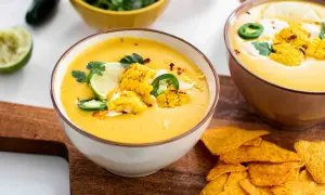 Zwei Schüsseln mit cremiger Mais-Suppe, garniert mit Maiskolben, Limette und Jalapeños, daneben Tortilla-Chips.