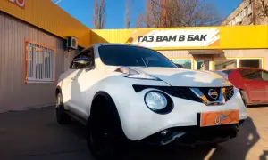 Biały Nissan Juke 1.6 benzyna z czarnymi felgami przed budynkiem z żółtym banerem "GAZ WAM W BAK".