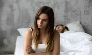 Een vrouw zit met gekruiste armen, gefrustreerd, terwijl haar partner slaapt. Ze probeert zich in te leven in anderen, maar voelt zich alleen.