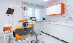 Nowoczesny gabinet stomatologiczny z fotelem dentystycznym w kolorze pomarańczowym i białymi meblami.