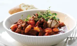 En skål med mustig chili con carne, garnerad med färska örter och en hel vitlöksklyfta. En bit bröd syns i bakgrunden.