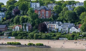 Prächtige Villen und grüne Hügel über einem Sandstrand an den Elbvororten Hamburgs. Menschen genießen den sonnigen Tag am Wasser.