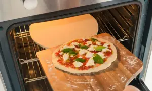 Przygotowania do dnia pizzy 2026: świeża pizza z mozzarellą i bazylią wsuwana na rozgrzany kamień w piekarniku.