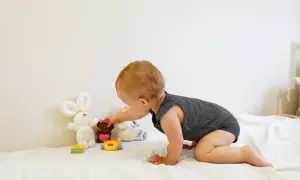 A baby explores Montessori baby activities, reaching for a teddy bear among soft toys on a white blanket.