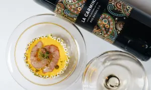 Elegancka butelka wina La Carmina i wykwintne danie z krewetką, ozdobione kwiatami. Idealny concord na wyjątkowy wieczór.