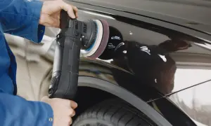 Osoba w niebieskiej kurtce poleruje czarne auto maszyną, pokazując jak usunąć rysy z auta.