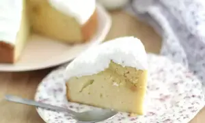 En saftig bit tres leches-kaka med fluffig vit topping, serverad på en blommig tallrik med en sked.