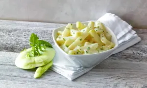 Kohlrabi kochen: zarte Kohlrabistücke in cremiger Sauce mit frischer Petersilie, daneben ein roher Kohlrabi.