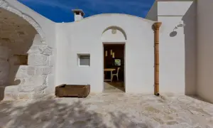 Interni di trulli pugliesi: un'apertura bianca rivela una sala da pranzo accogliente, con un camino e un piccolo orto in pietra all'esterno.