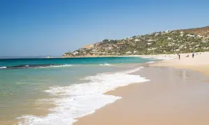 Aguas turquesas y arena dorada en las calas de Tarifa, con casas blancas salpicando la ladera verde. Un día perfecto para disfrutar del mar.