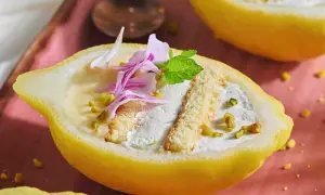 Delizia al limone: crema soffice e biscotti in un limone scavato, guarnito con pistacchi e petali rosa.
