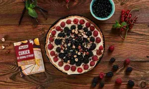 Pyszna tarta z mascarpone, malinami, jeżynami i borówkami, posypana orzechami. Obok opakowanie cukru z skórką cytrynową.
