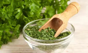 Prezzemolo essiccato in una ciotola di vetro, con un mestolo di legno. Un'erba aromatica utile anche in gravidanza.