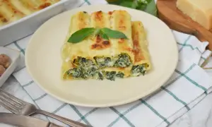 Pyszne cannelloni ze szpinakiem, zapieczone pod beszamelem i serem, ozdobione listkiem bazylii.