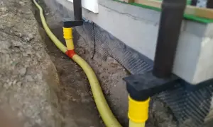 System odprowadzenia wody z rynny, z żółtą rurą biegnącą w wykopie przy fundamencie.
