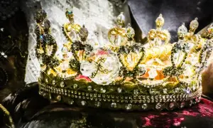 Korona zdobiona klejnotami, symbol bogactwa i władzy, przypomina o globalnym wydobyciu złota.