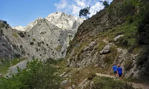 Dos niños disfrutan de la ruta Poncebos - Bulnes con niños, caminando por un sendero rocoso entre imponentes montañas.
