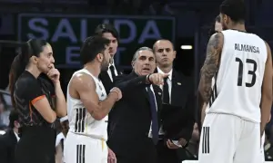 Entrenador del r madrid baloncesto señala una jugada. Jugadores y árbitra observan.