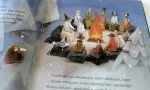 Ilustracja przedstawia grupę ludzi siedzących wokół ogniska, z dzieckiem przykrytym kocem po lewej stronie.