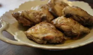 Un plat de haut de cuisse de poulet rôti, assaisonné d'herbes, servi sur une assiette en céramique crème.