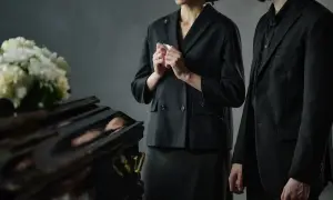 Elegancki ubiór damski na pogrzebie latem: czarna marynarka, spódnica i kapelusz. Obok trumna i bukiet białych kwiatów.