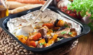 Szybkie danie z piekarnika: pieczone warzywa korzeniowe, dynia i mięso w folii aluminiowej, gotowe do podania.