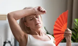 Frau fächelt sich mit einem orangefarbenen Fächer Luft zu, um etwas gegen Hitzewallungen zu tun.
