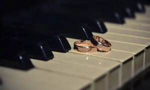 Dos alianzas de oro descansan sobre teclas de piano, evocando la pregunta: ¿cuanto pesa una alianza de oro?