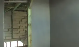 Ściana z tynkiem cementowo-wapiennym i widok na budowę w tle.