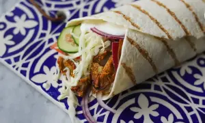 Pyszny kebab w picie z soczystym mięsem, chrupiącą surówką, pomidorem, ogórkiem i czerwoną cebulą, zawinięty w ciepły placek.