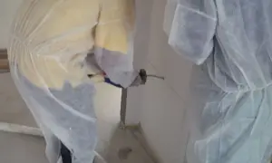 Dos operarios con trajes protectores aplican espuma intumescente en una pared, sellando una junta para protección contra incendios.