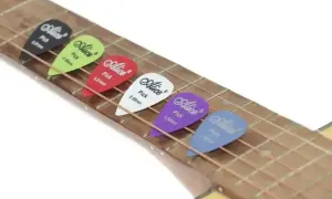 Kolorowe kostki do gry na gitarze Alice leżą na strunach. Każda kostka ma inny kolor i grubość.