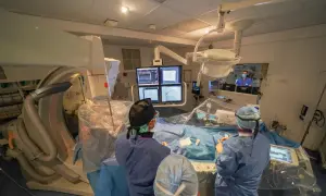 Équipe médicale en salle d'angiographie, préparant le repos après une coronarographie. Moniteurs affichant des images cardiaques.