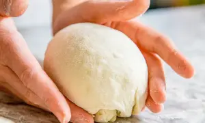 Hände formen einen Teigball auf einer bemehlten Oberfläche.