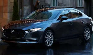 Elegancka, ciemnoszara Mazda 3 sedan stoi na mokrej ulicy, odbijając światła miasta.