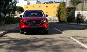 Czerwona Mazda CX-5 jedzie ulicą. W tle budynki i drzewa.
