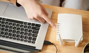 Ręka wskazuje na router, podłączony kablem USB do laptopa. Dowiedz się, jak połączyć falownik z wifi.