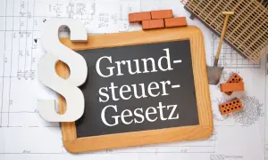 Ein Paragrafensymbol und eine Tafel mit "Grundsteuer-Gesetz" liegen auf Bauplänen. Ziegel und Werkzeug deuten auf den Grunderwerbsteuer in Niedersachsen hin.