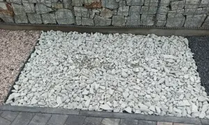 Biały grys, czyli drobne, łamane kamienie, tworzy jasną powierzchnię obok gabionów i ciemniejszego kamienia.