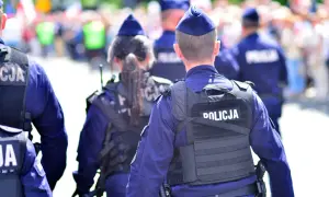 Policjanci w mundurach, tworzący zgraną kartę rodziny mundurowej, patrolują ulicę. Na kamizelkach taktycznych widnieje napis "POLICJA".