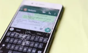 Pęknięty ekran telefonu wymaga pilnej wymiany. Widać klawiaturę i fragmenty rozmowy.