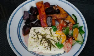 En tallrik med ugnsbakade rödbetor, sötpotatisstavar och en stor bit fetaost i ugn, toppad med örter. Serveras med en fräsch sallad.