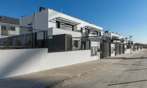 Modernos chalets adosados blancos con vallas metálicas y puertas de garaje.