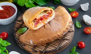 Pyszny calzone przepis: złociste ciasto z sosem pomidorowym i serem, podane z pomidorkami i bazylią.