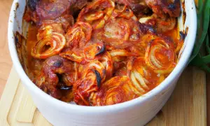 Pieczona karkówka z cebulą w sosie pomidorowym w naczyniu żaroodpornym.