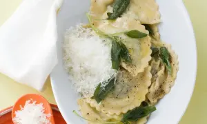 Ravioli mit Spinat-Ricotta-Füllung, Salbeiblättern und geriebenem Parmesan auf einem Teller.