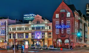 Polizeigebäude und St. Pauli Theater in Hamburg bei Nacht, mit leuchtenden Schildern und Autos.