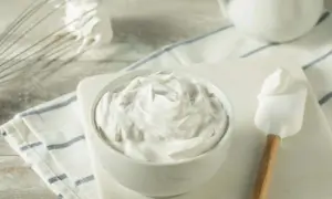 Puszysta śmietana w misce, obok ubijaczka i szpatułka. Idealna do deserów, zastanawiasz się, ile żelatyny na pół litra śmietany?