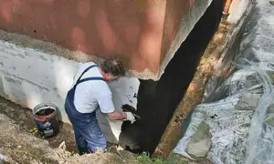 Mann trägt Bitumenanstrich innen auf die Kellerwand auf.