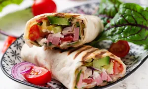 Pyszna tortilla z szynką, awokado, pomidorami i serem feta, podana z sałatką i czerwoną cebulą.